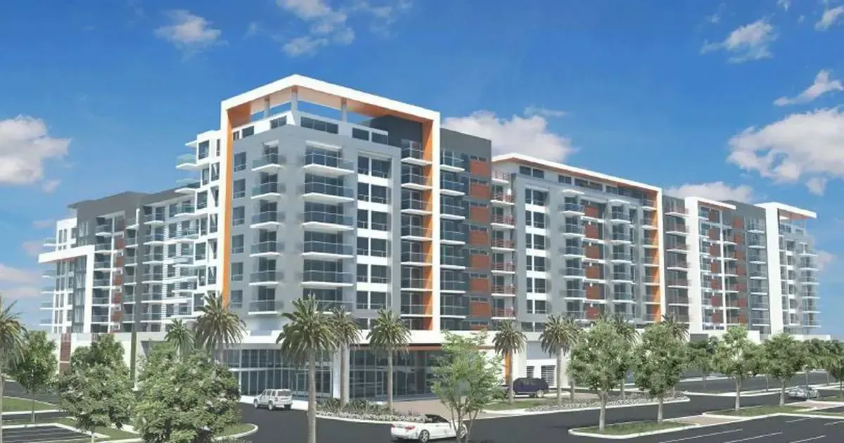 Modern multi-story apartment building with balconies, orange accents, and palm trees along a street
