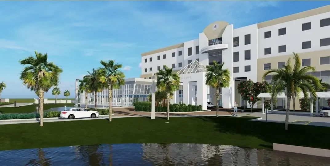 Modern white hotel with palm trees and lawn reflected in water under a blue sky