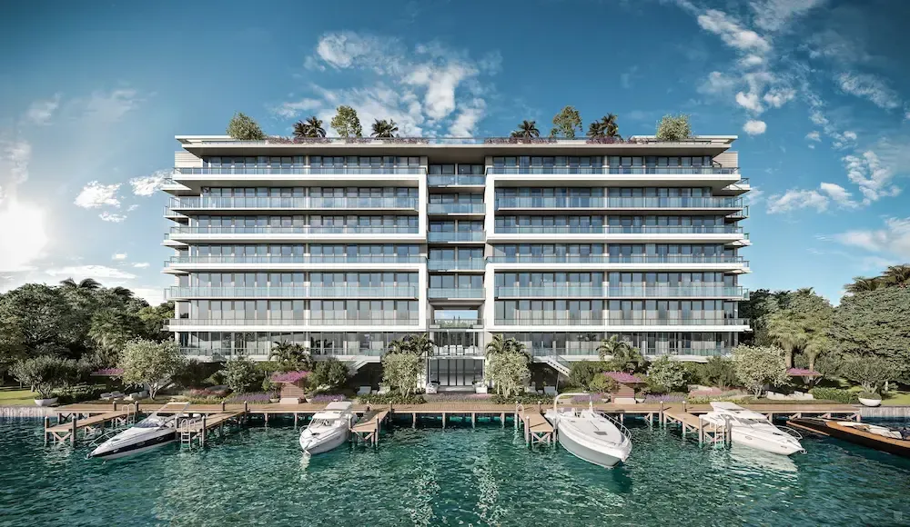 Modern waterfront hotel with balconies, lush greenery, and boats docked on turquoise water