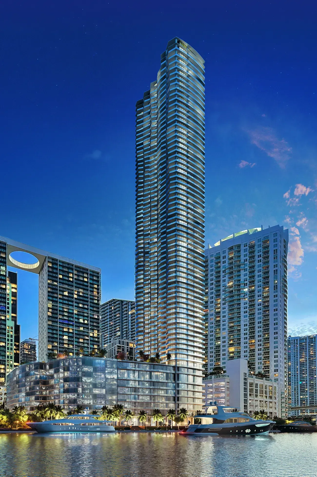 Tall illuminated waterfront skyscraper at dusk with neighboring high-rises and reflections on the water