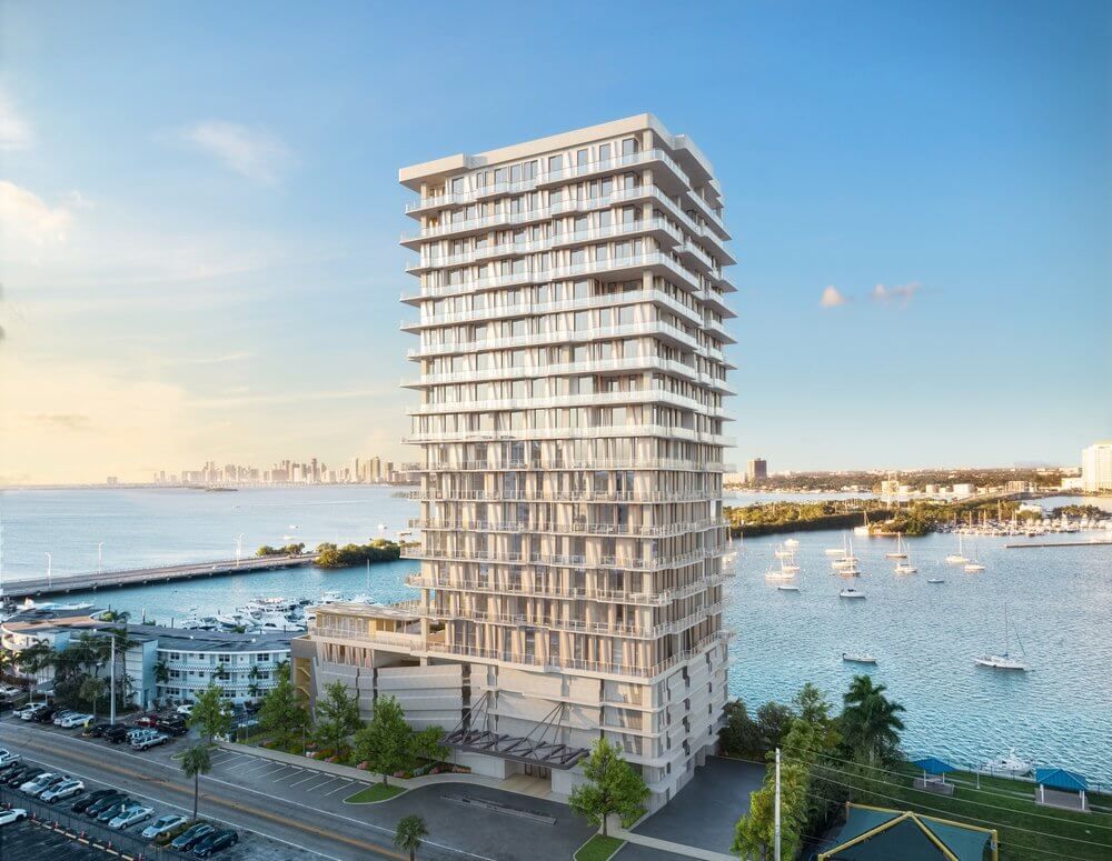 Tall modern waterfront apartment tower beside a marina under a clear blue sky