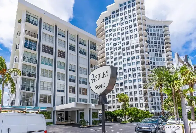 Modern white hotel towers with palm trees and a sign reading “Ashley 2080” on a sunny street.