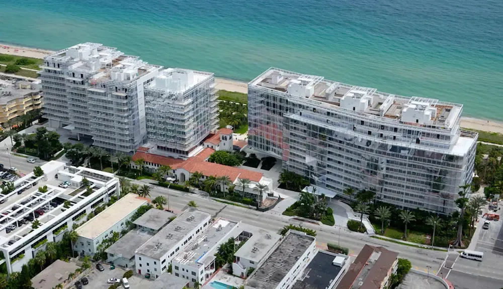 Aerial view of two modern beachfront apartment buildings beside a road and turquoise ocean.
