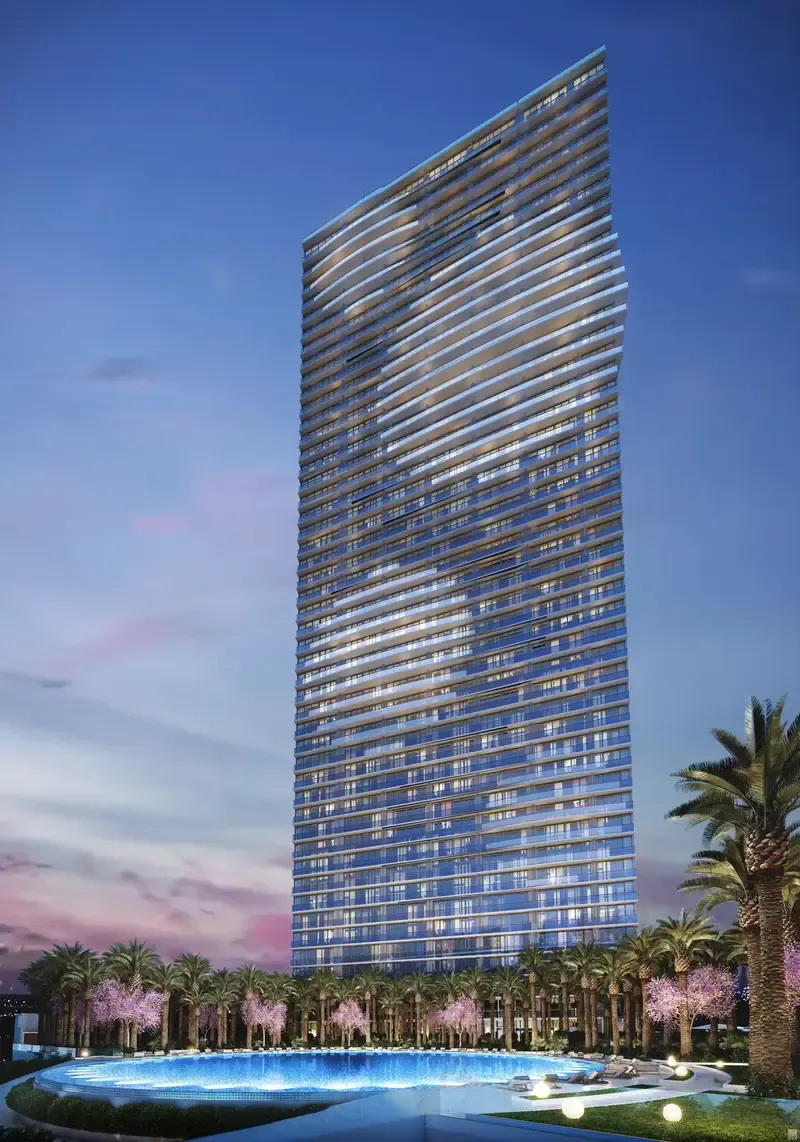 Tall glass skyscraper at dusk beside a lit pool and palm trees