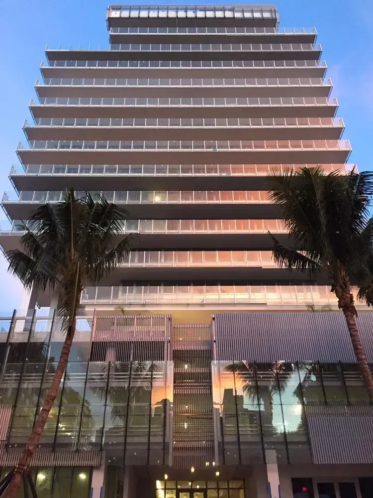 Modern high-rise building at dusk, with palm trees and illuminated glass facade