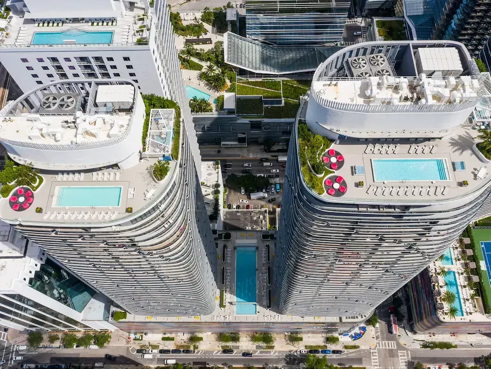 Aerial view of two curved rooftop towers with pools, surrounded by modern city buildings.