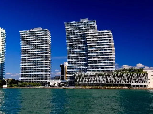 Modern waterfront high-rises with balconies beside turquoise water under a clear blue sky