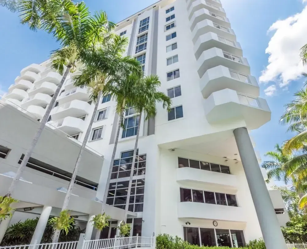 Modern white high-rise apartment building with balconies and palm trees under a blue sky