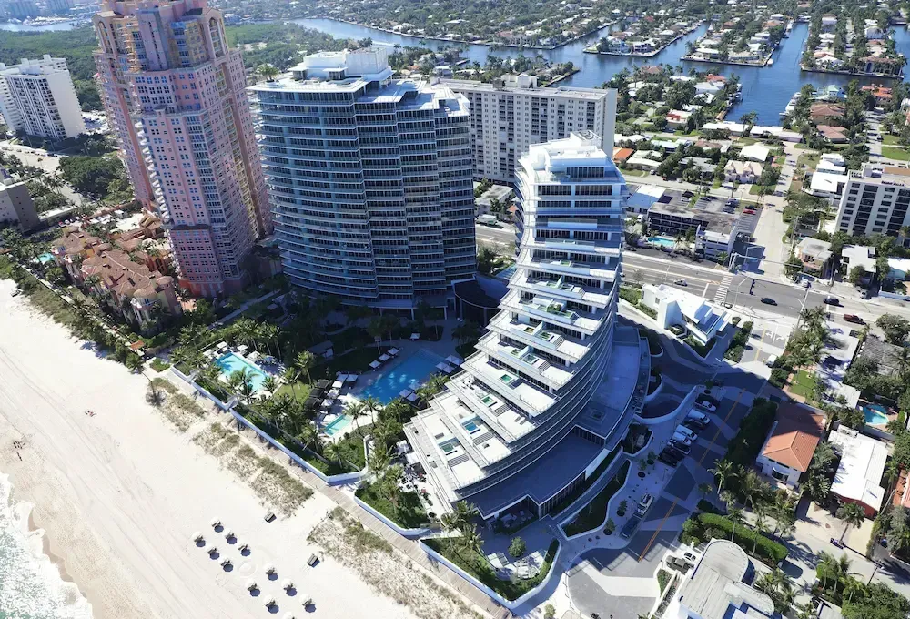 Aerial view of beachfront high-rises beside a sandy shore and marina-lined waterway.
