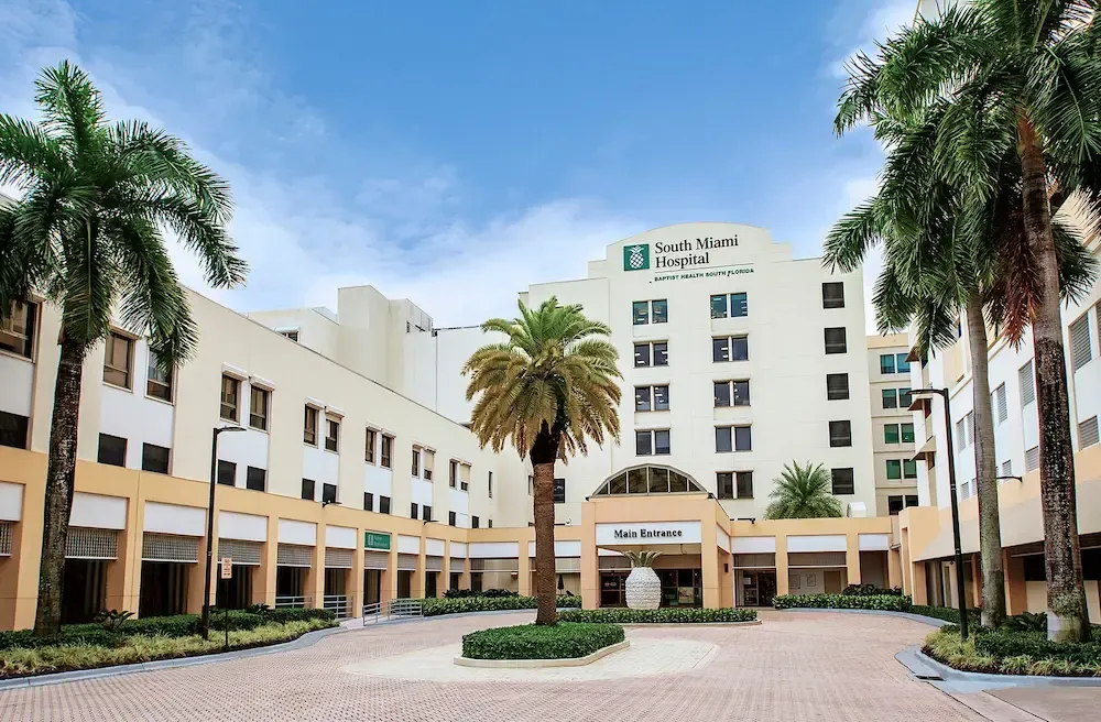 Modern hotel courtyard with palm trees, beige buildings, and a circular driveway under a blue sky