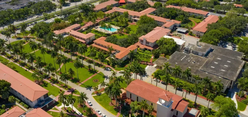 Aerial view of a campus with red-roofed buildings, palm trees, and walkways surrounded by greenery