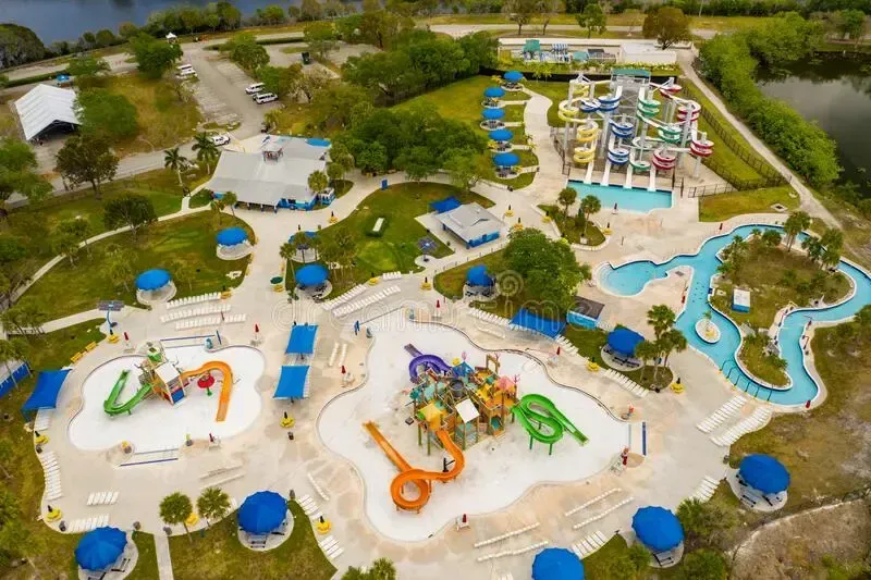 Aerial view of a colorful water park with slides, splash zones, pools, and blue umbrellas