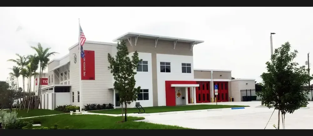 Modern two-story white building with red accents, glass entrance, and trees in front