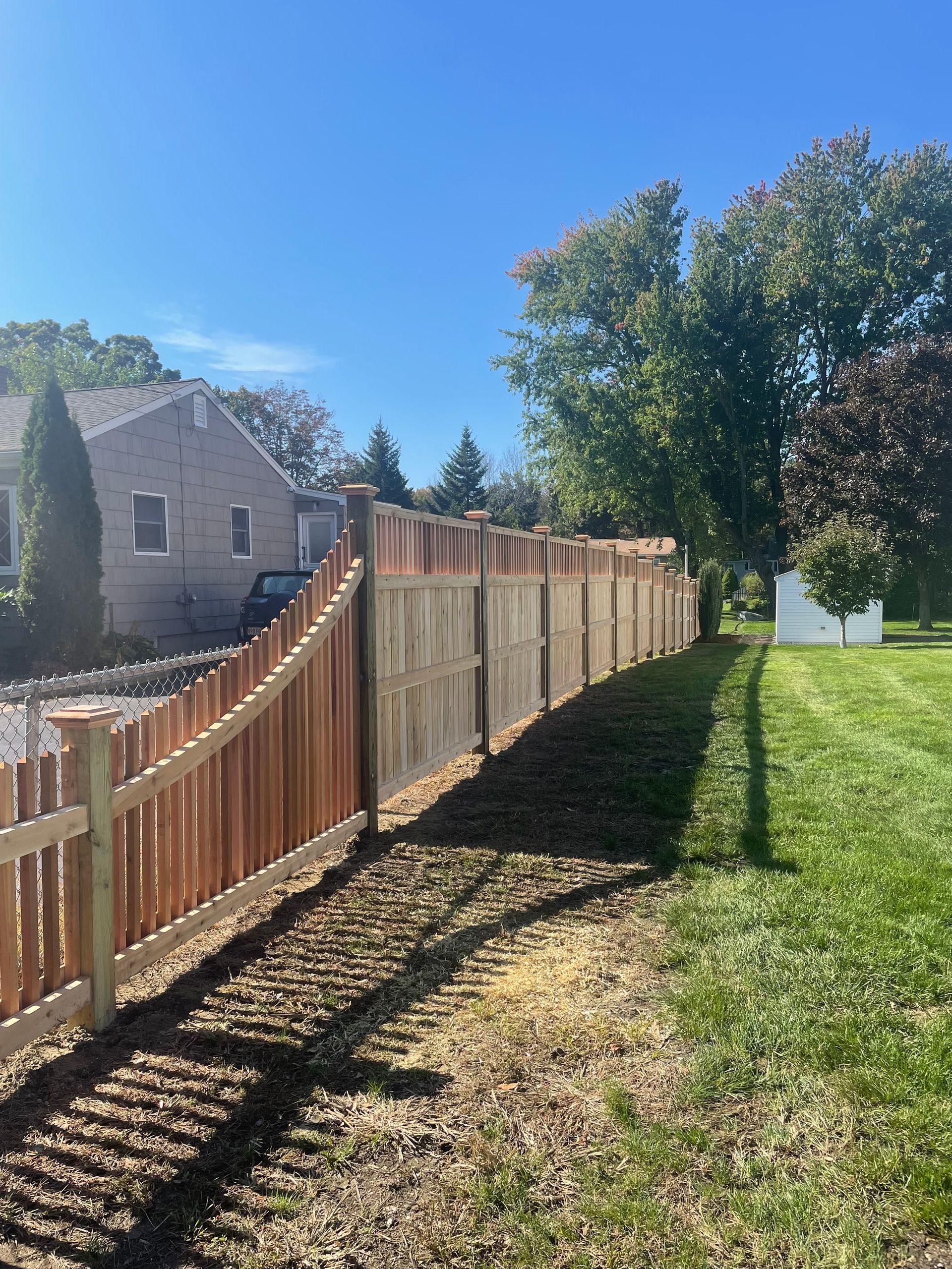 A wooden fence surrounds a lush green field in front of a house.
