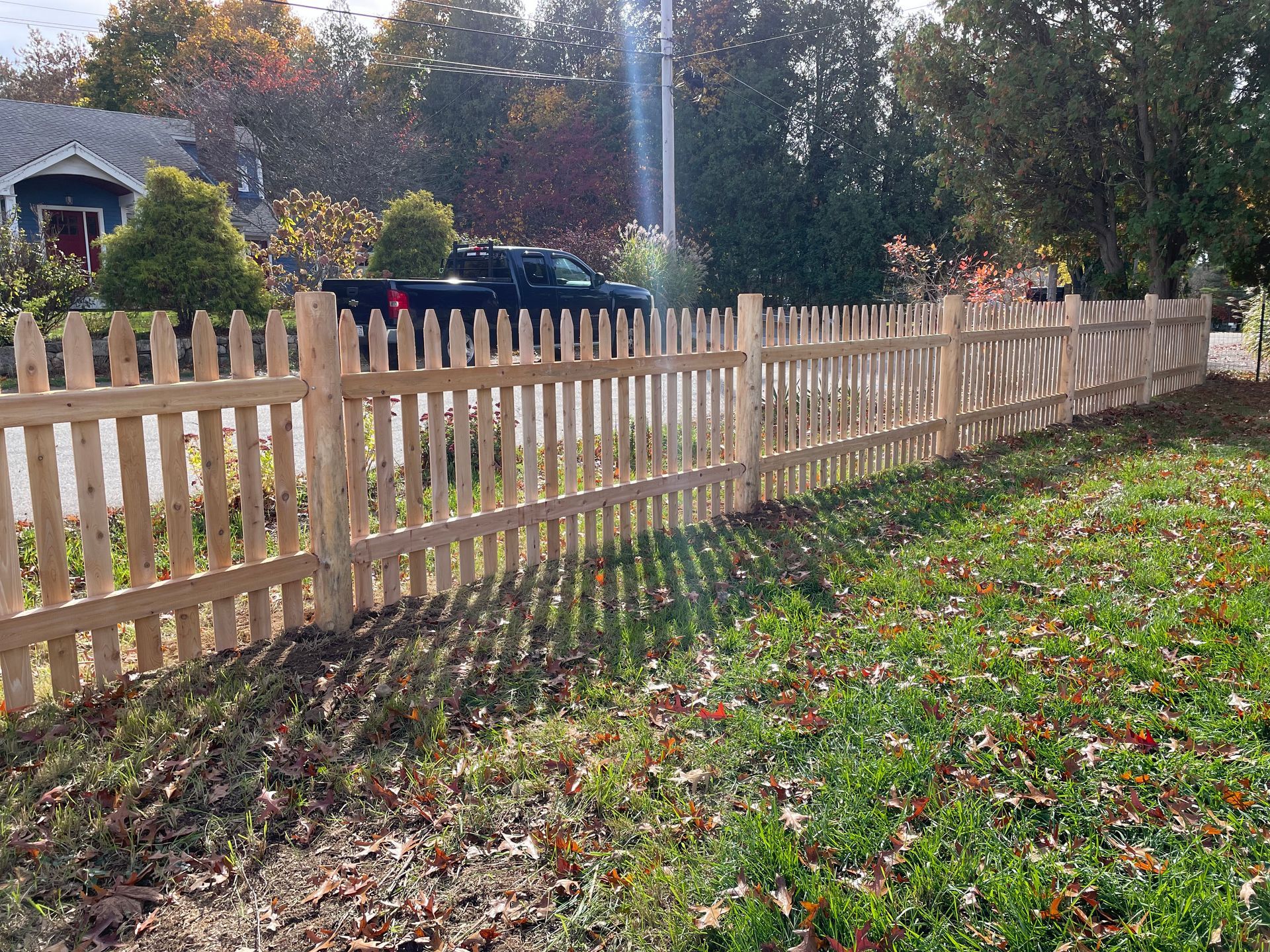 A wooden picket fence surrounds a grassy yard in front of a house.