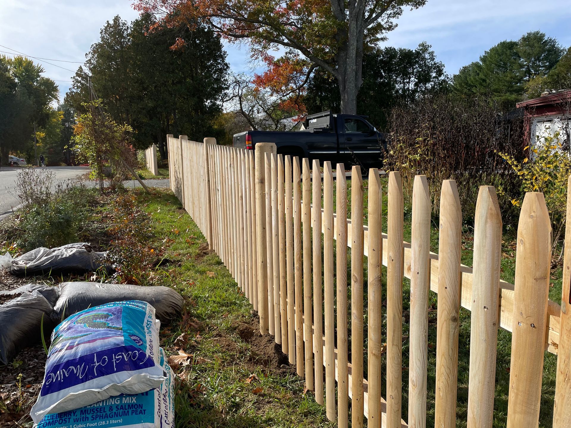 A wooden picket fence is sitting next to a bag of soil.