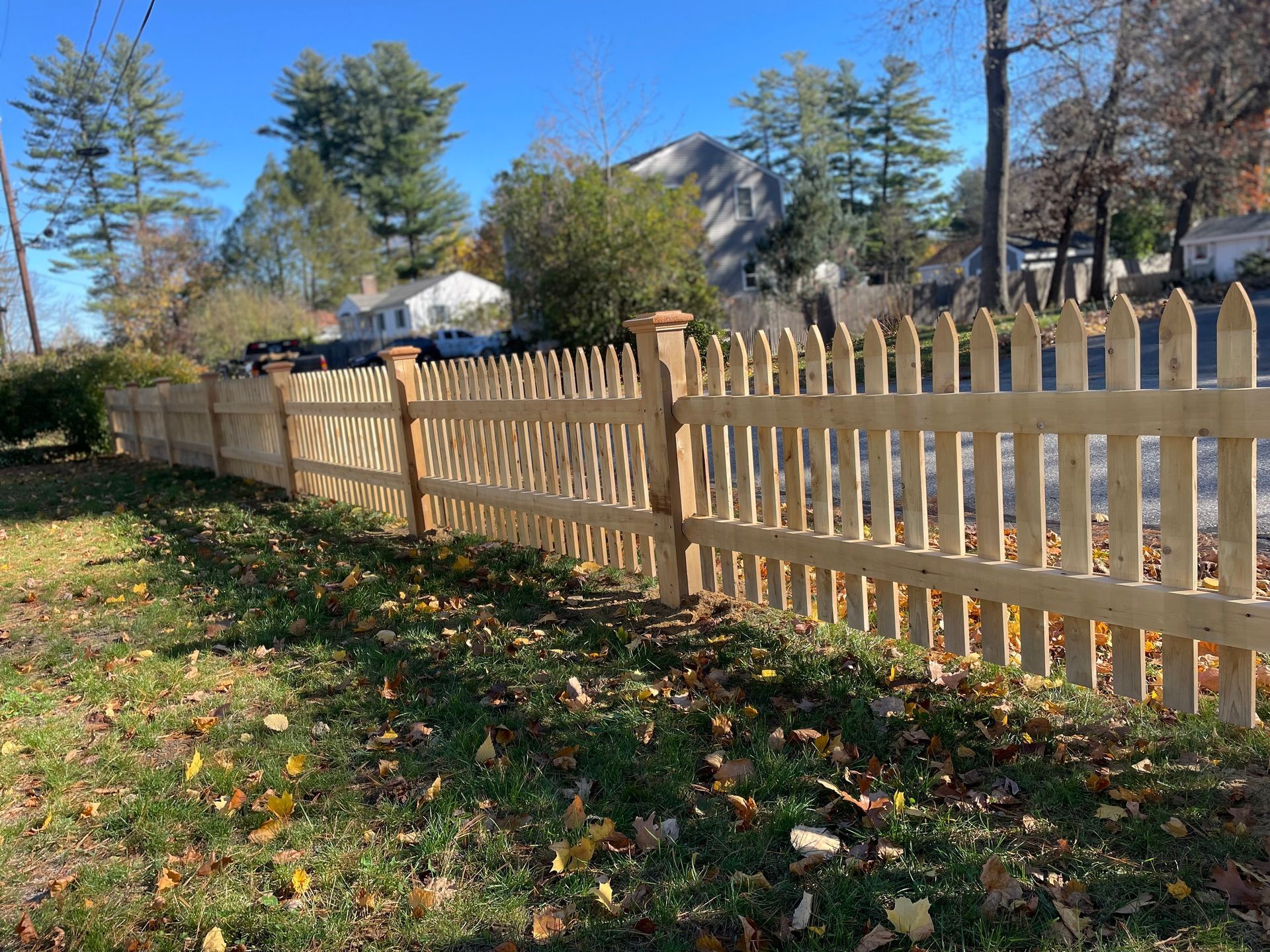 A wooden picket fence is surrounded by grass and trees in a yard.