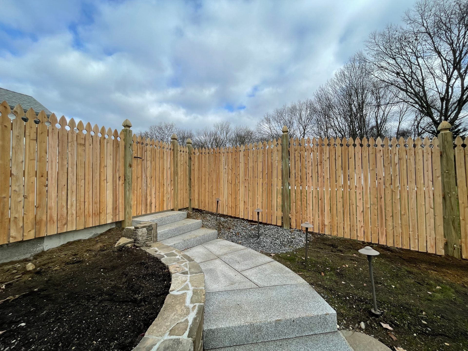A wooden fence surrounds a stone walkway in a backyard.