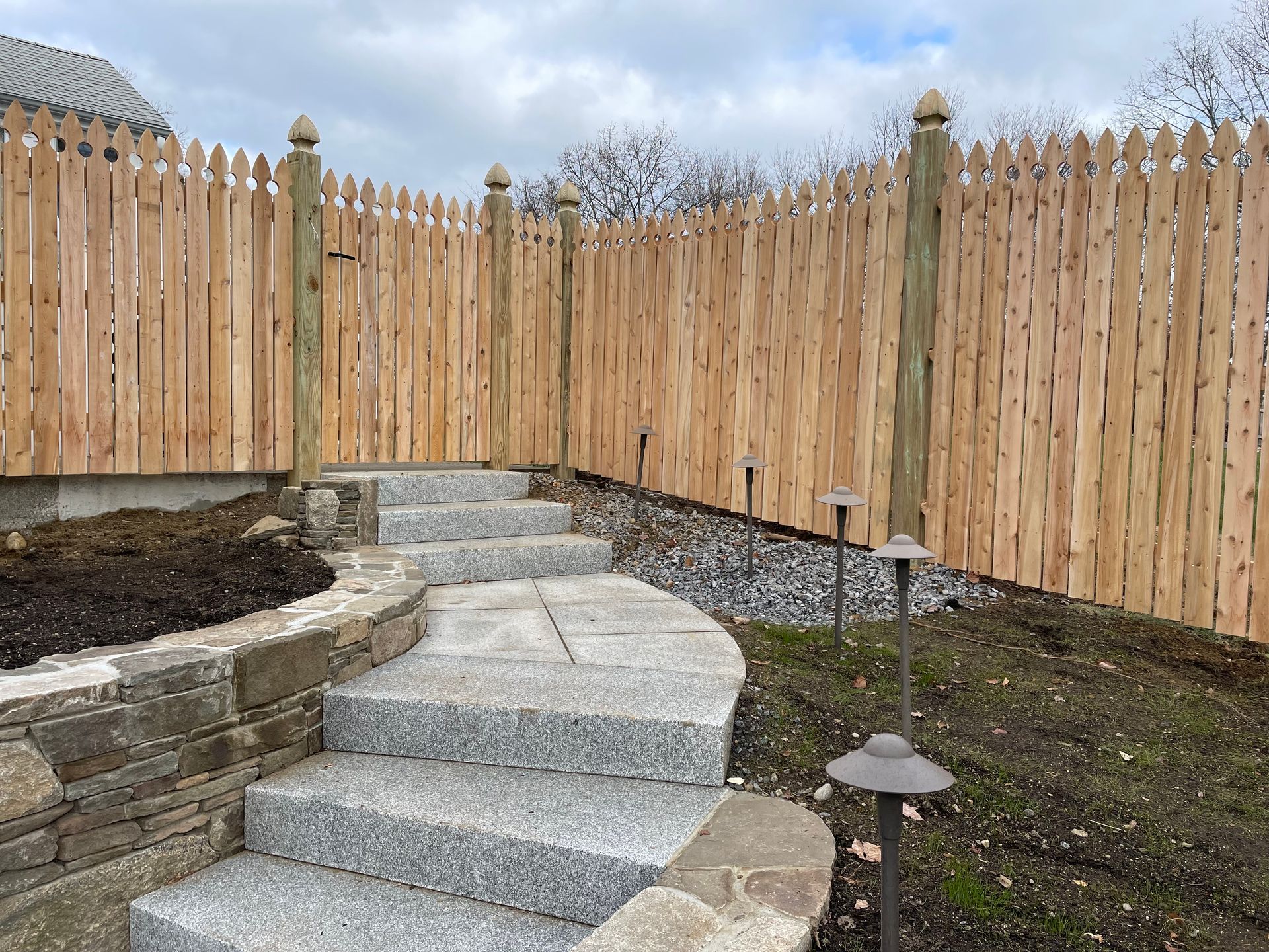 A wooden fence surrounds a stone walkway with stairs leading up to it.