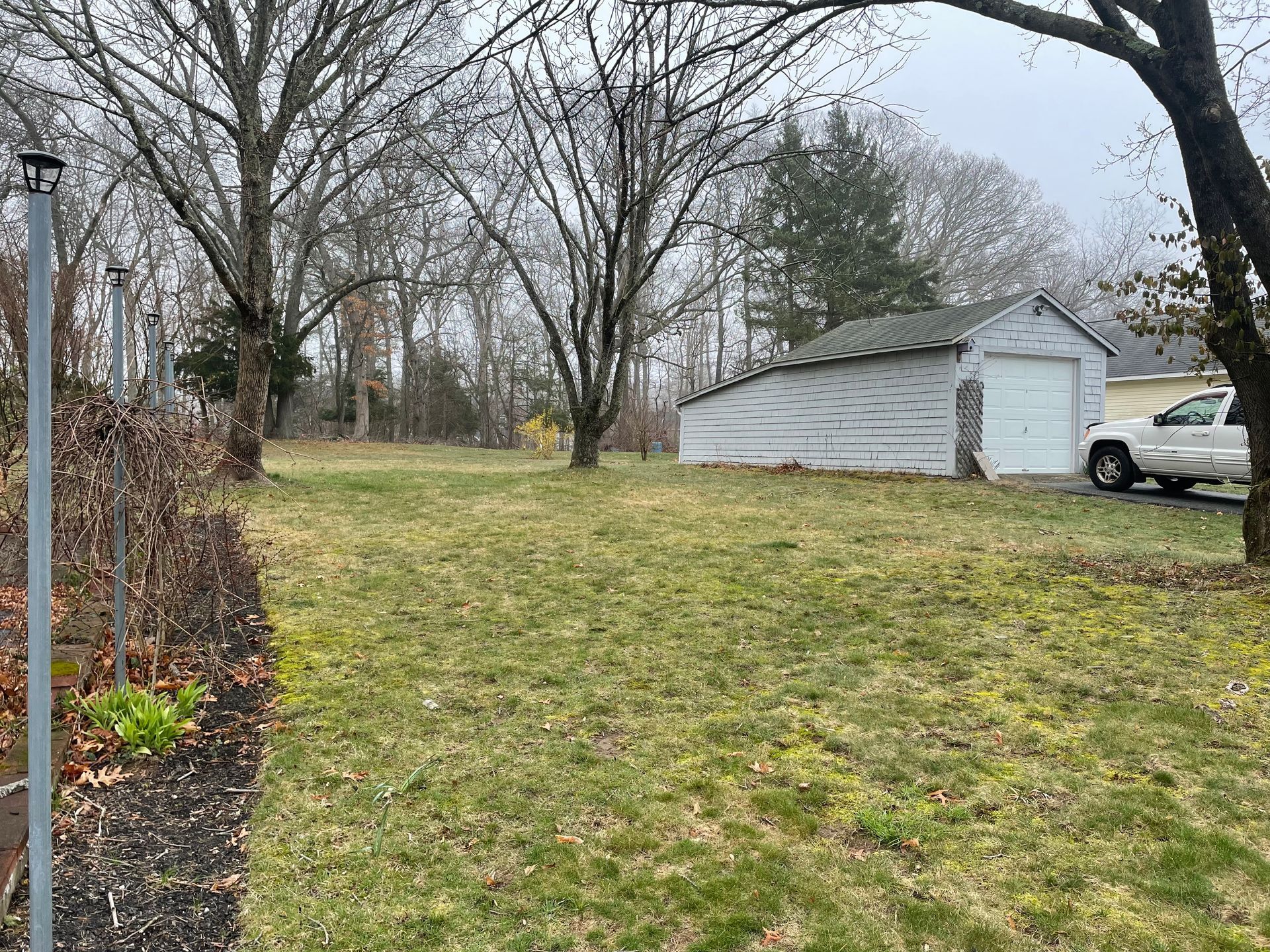A white truck is parked in a grassy yard next to a garage.