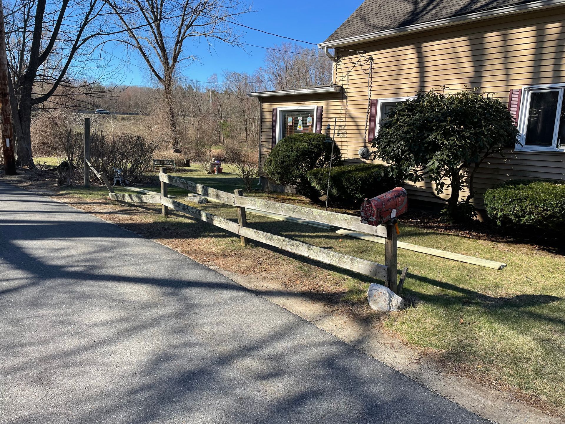 A wooden fence is along the side of a road in front of a house.