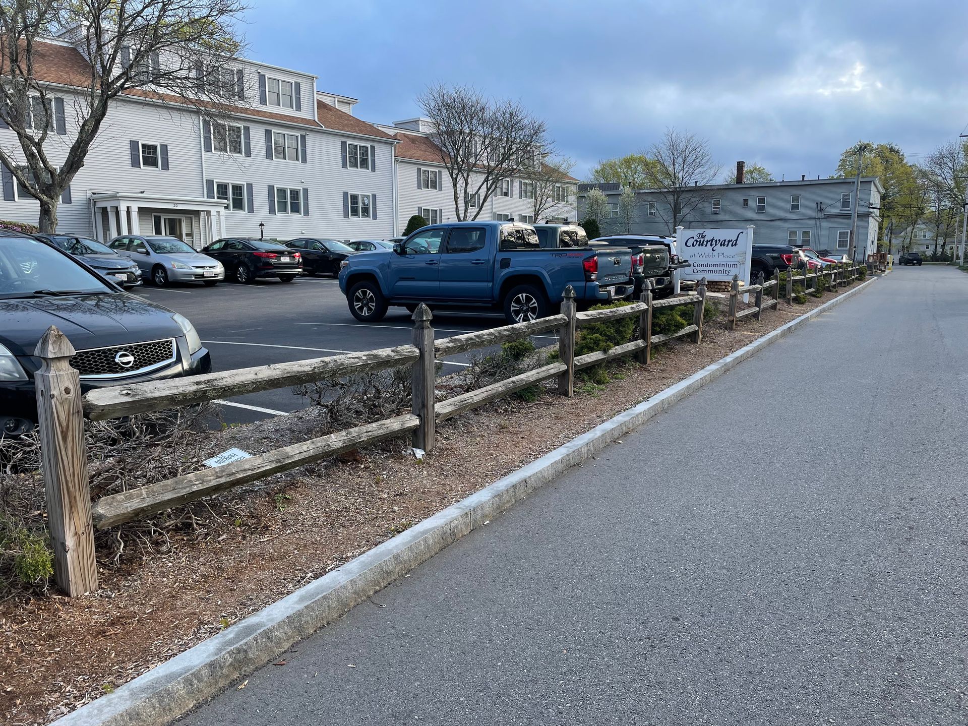 A blue truck is parked in a parking lot next to a wooden fence.