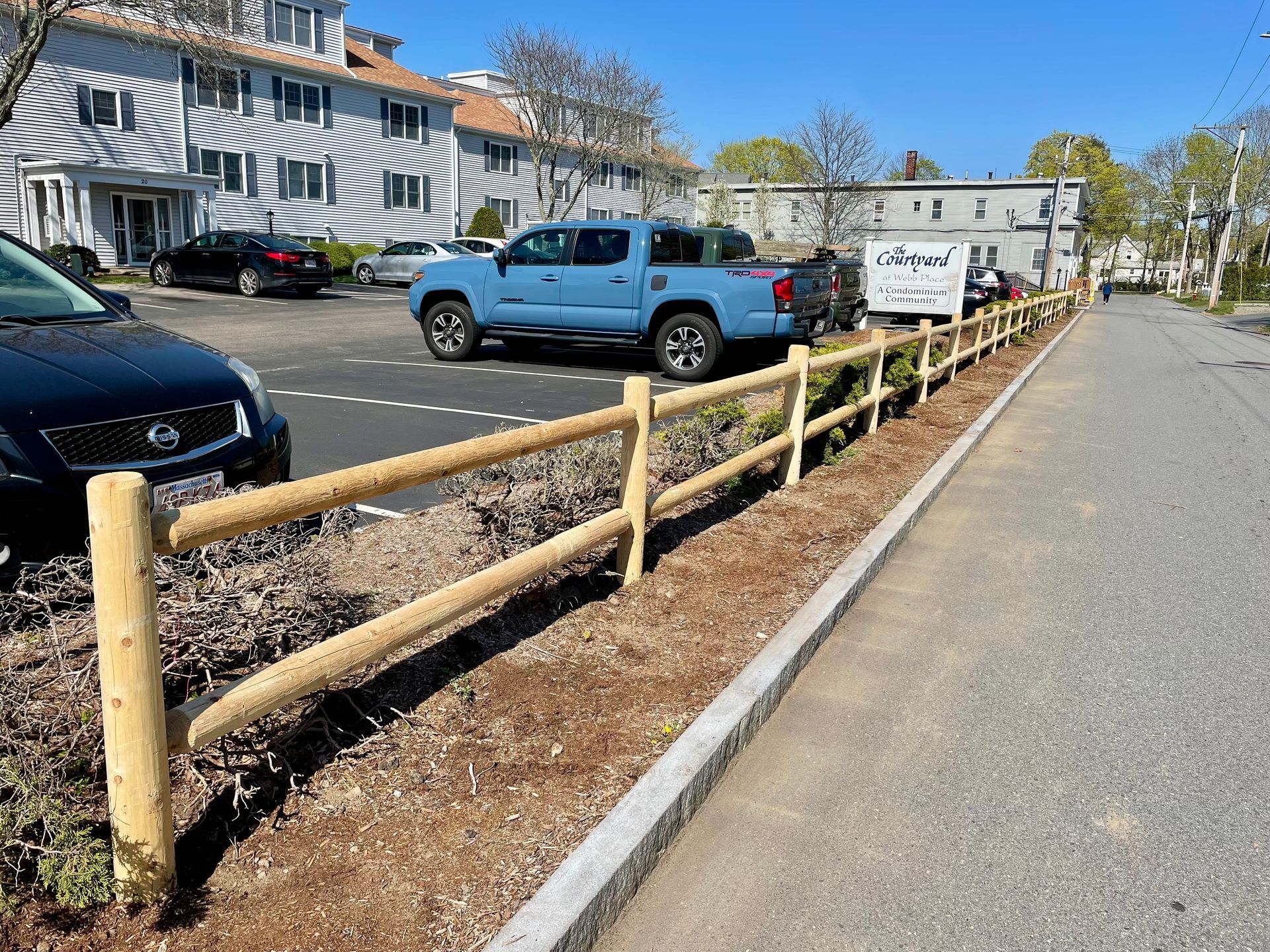 A blue truck is parked in a parking lot next to a wooden fence.