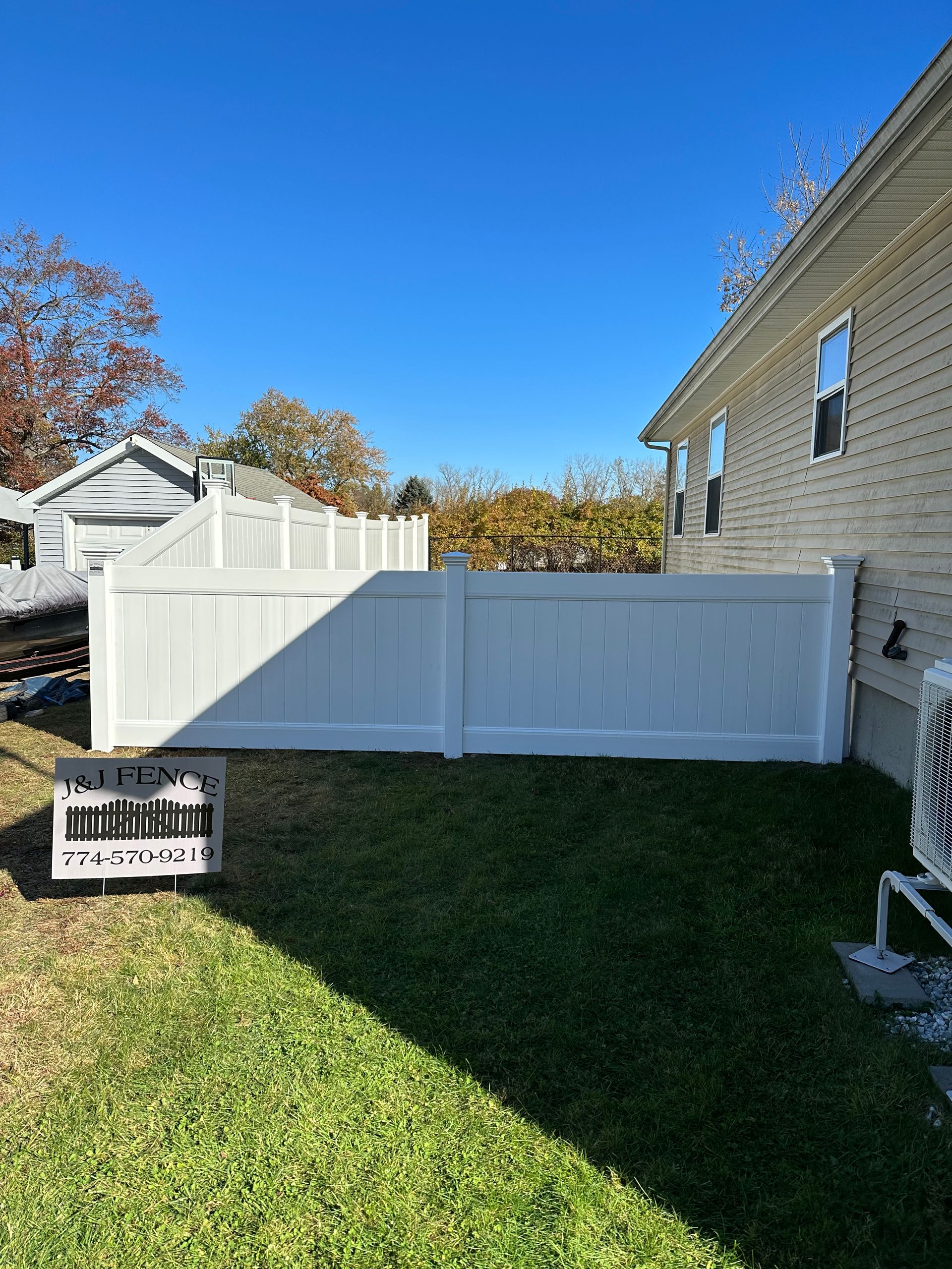 A white vinyl fence is in the backyard of a house.