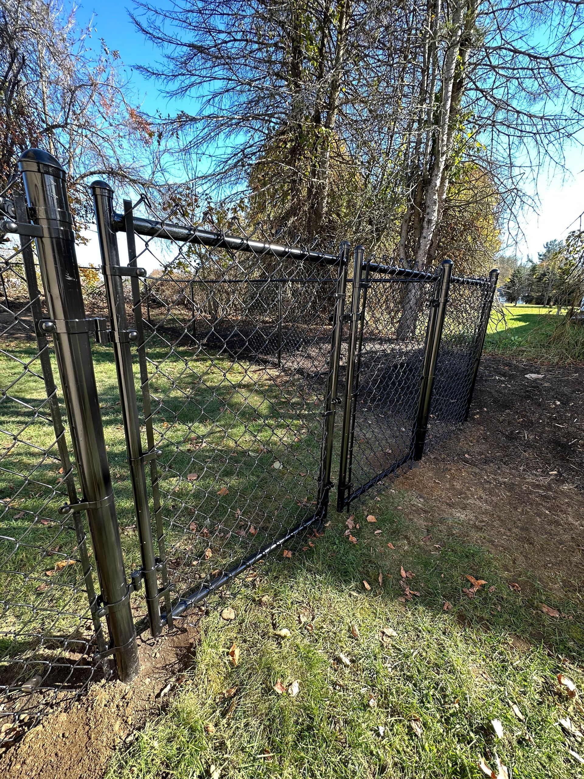 A chain link fence is surrounded by grass and trees in a park.