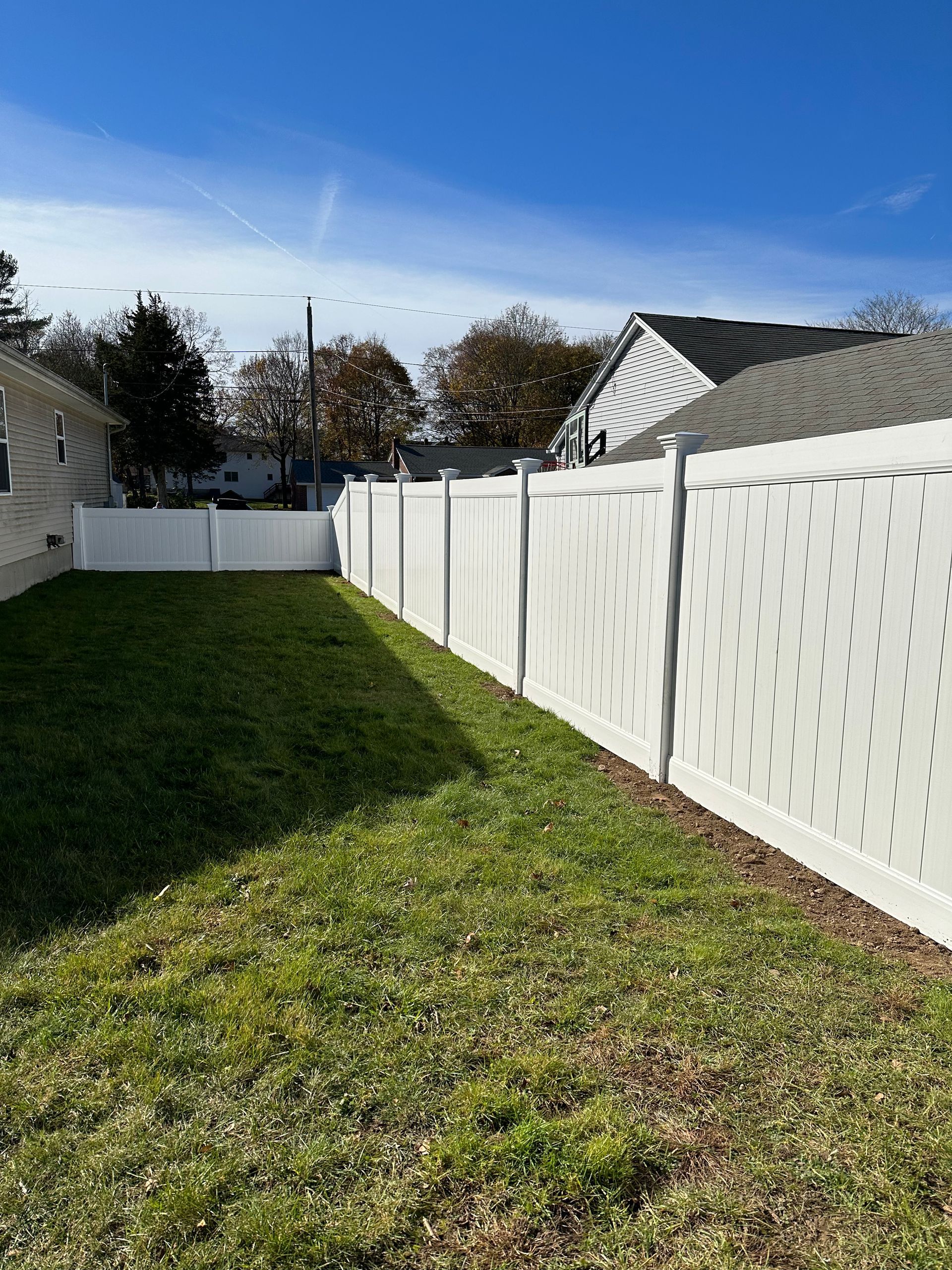 A white fence surrounds a lush green yard in front of a house.