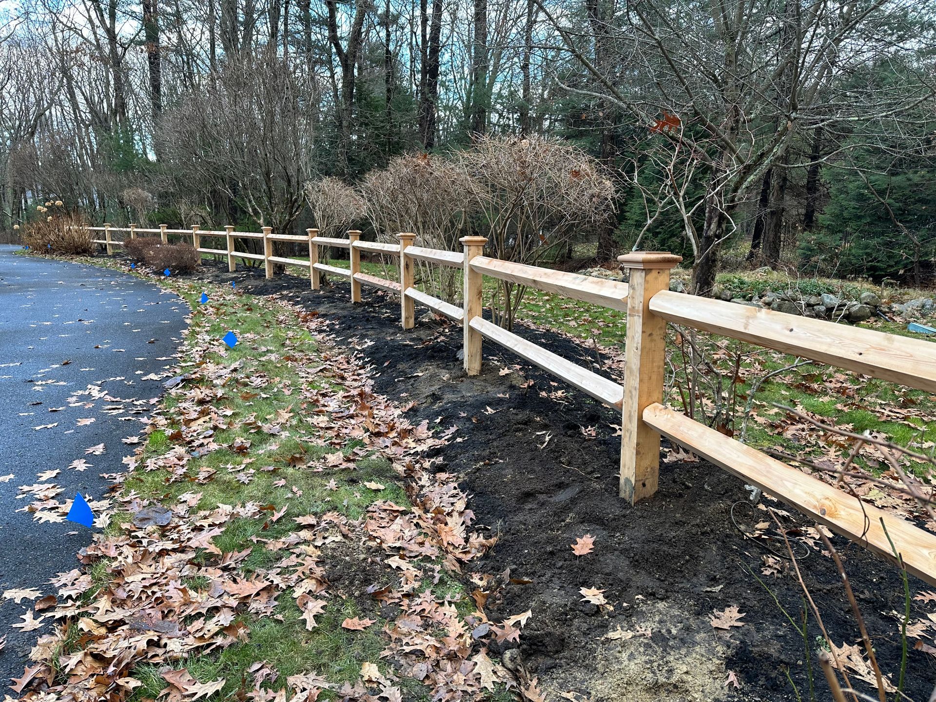 A wooden fence is sitting on the side of a road next to a forest.