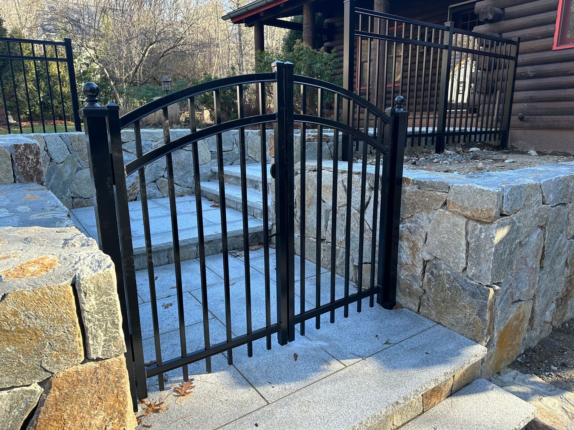 A black wrought iron gate is surrounded by stone steps and a stone wall.