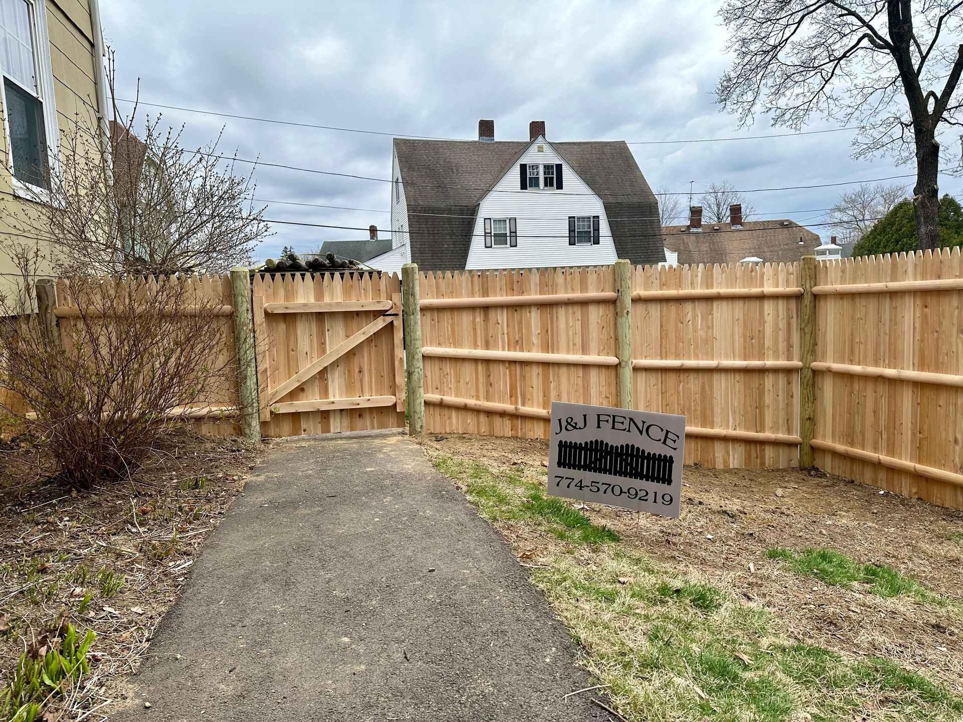 A wooden fence surrounds a path with a house in the background.