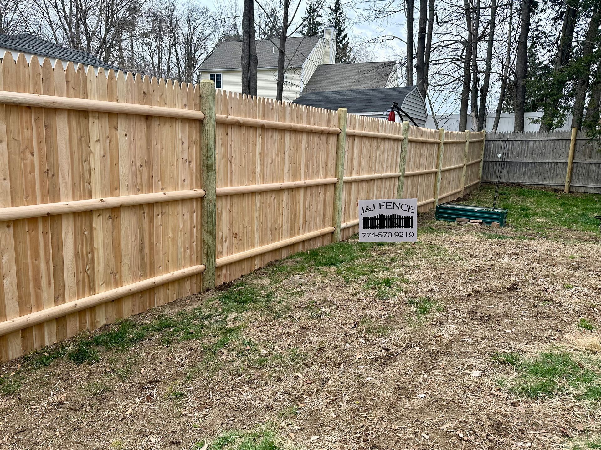 A wooden fence is sitting in the middle of a yard next to a house.