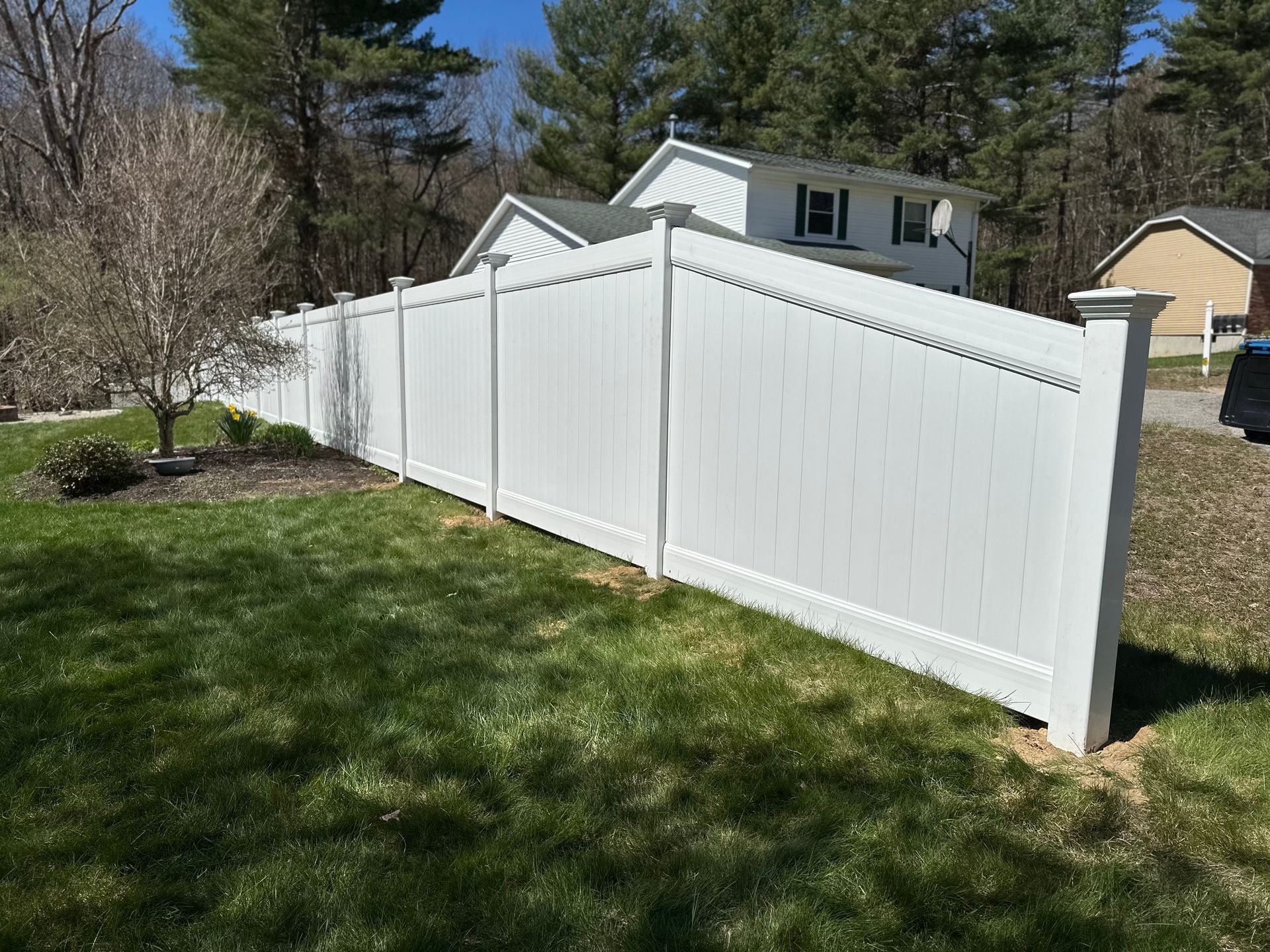A white fence is sitting in the grass in front of a house.