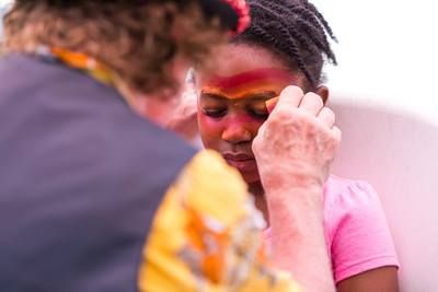 A person paints red and yellow designs on another individual's face using a small brush.