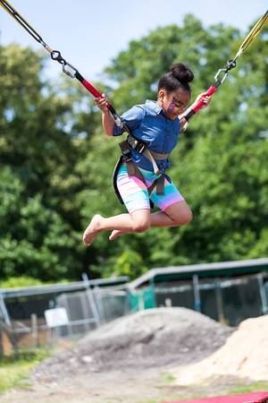 A person in a blue shirt and colorful shorts suspended in mid-air on a bungee trampoline ride outdoors.