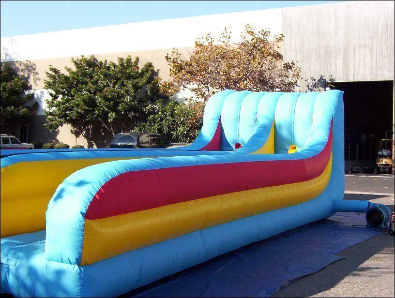 A long, inflatable blue, yellow, and red obstacle course game set up outdoors on a paved lot.
