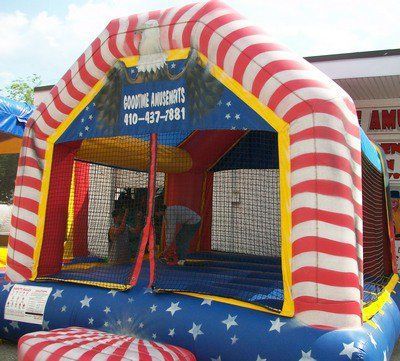 A red, white, and blue inflatable bounce house with a patriotic eagle design and a phone number on the front panel.