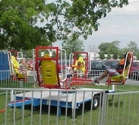 Children ride a red and yellow rotating amusement park ride outdoors on a grassy field.