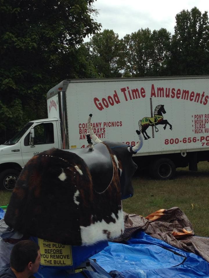 A mechanical bull in an outdoor field with a Good Time Amusements truck parked in the background.
