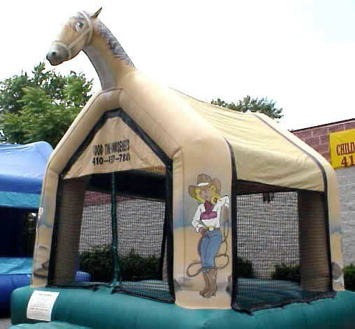A tan, horse-shaped inflatable bounce house with a cartoon cowgirl illustration, outdoors near a brick building.