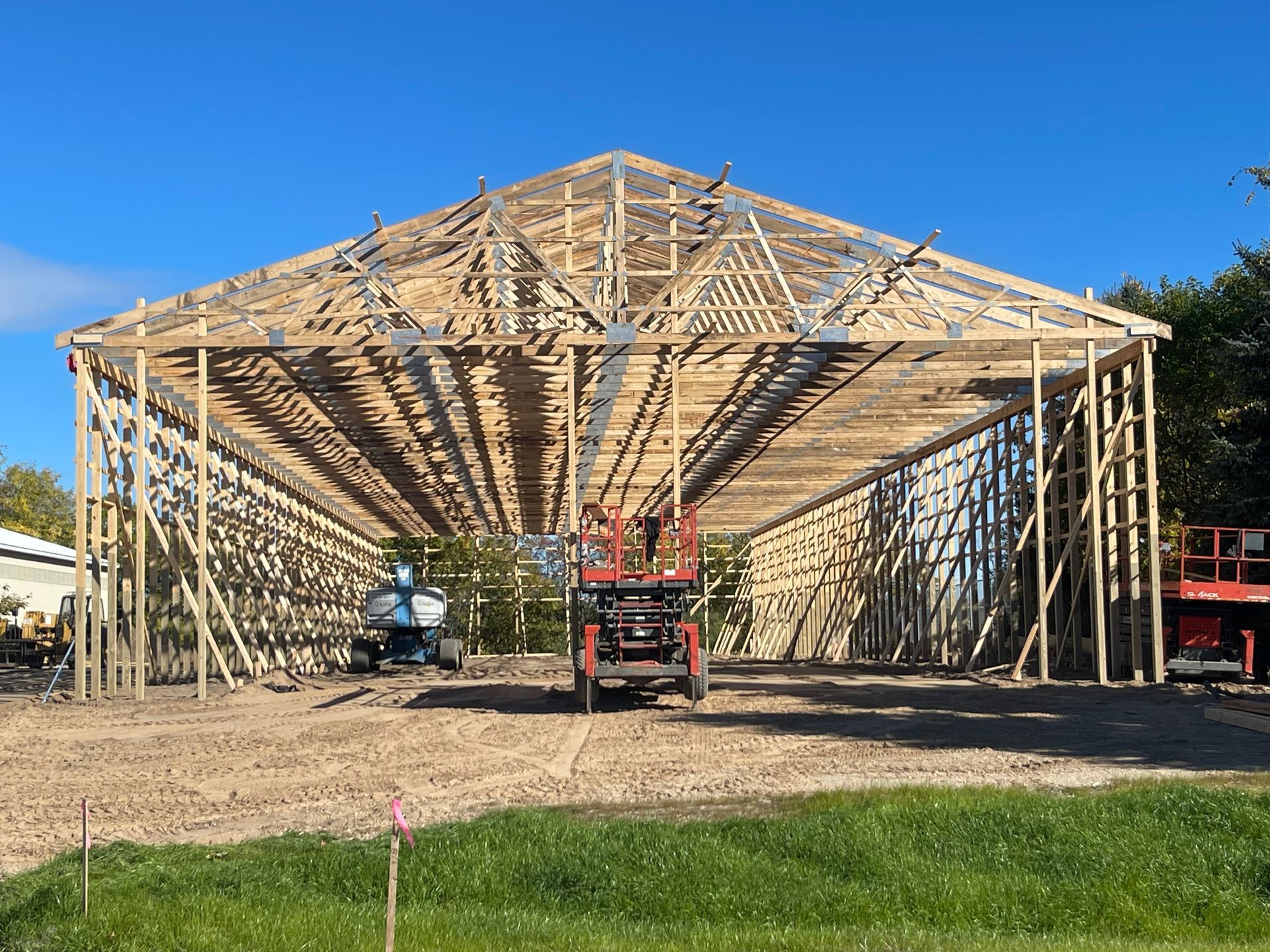 Construction site, wooden frame of a large building under a blue sky, with lift equipment in front.