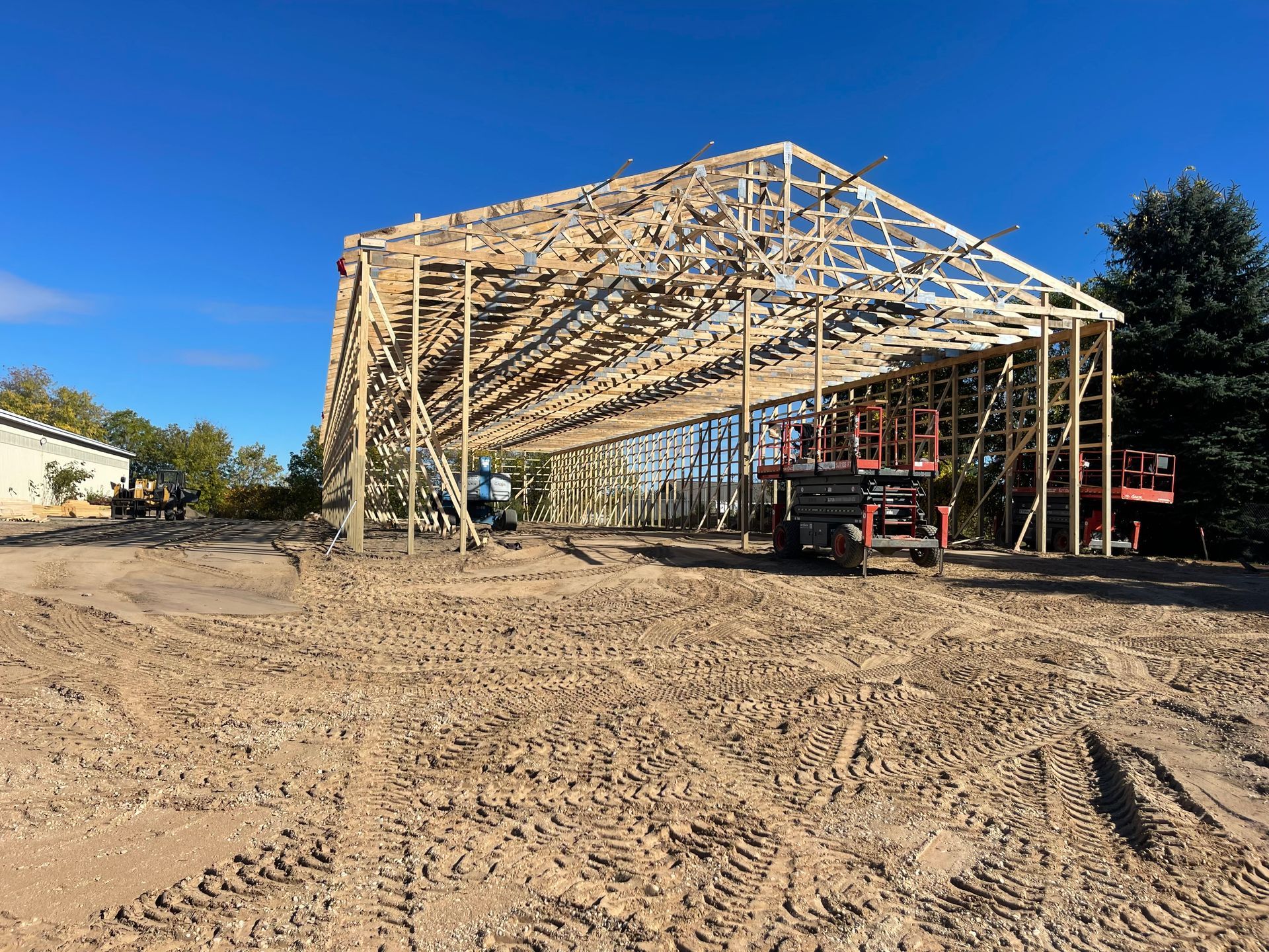 Wooden structure of a building under construction on a dirt lot, blue sky.