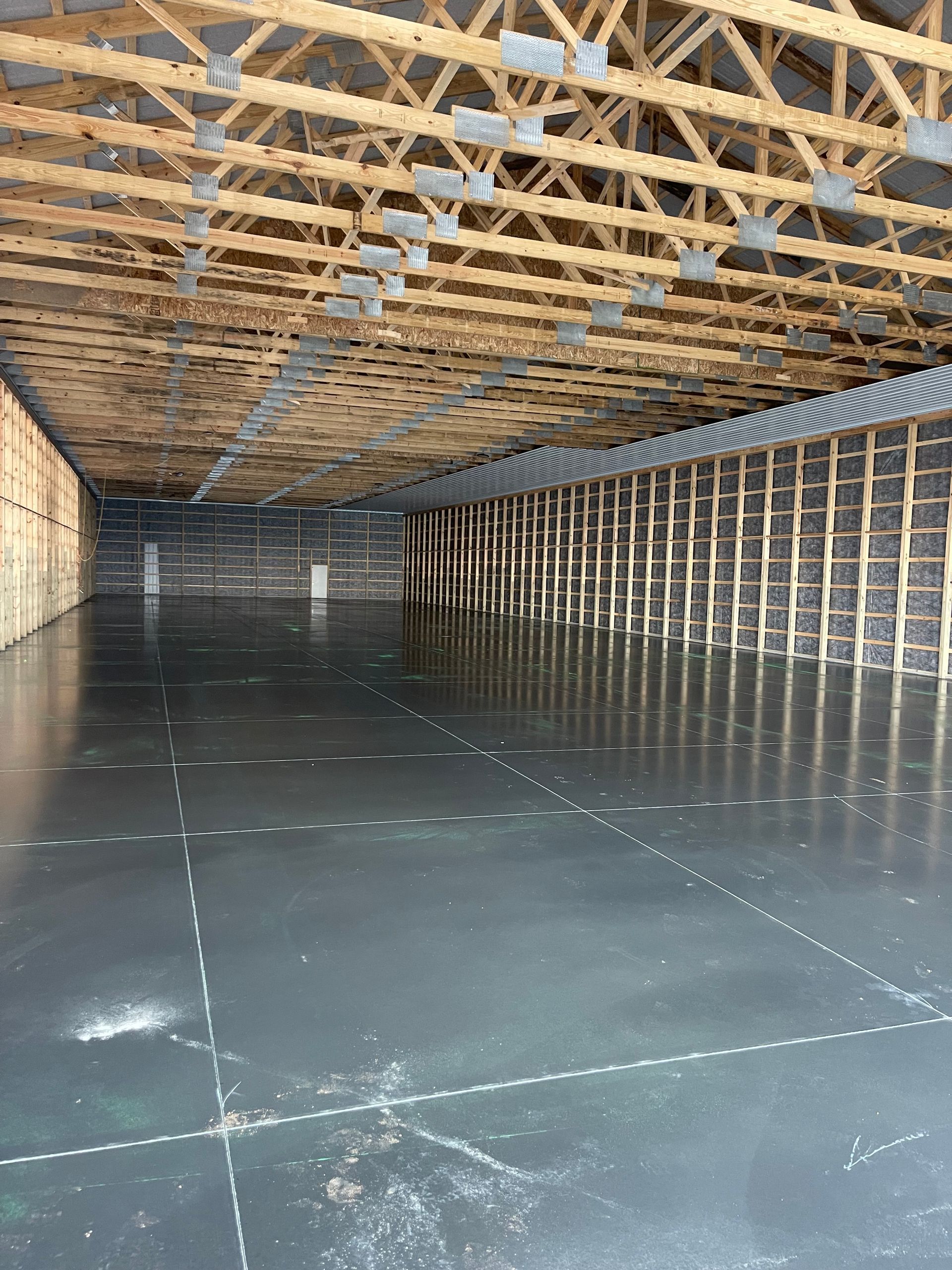 Empty, newly constructed warehouse interior. Concrete floor, wooden beams, and walls with insulation visible.