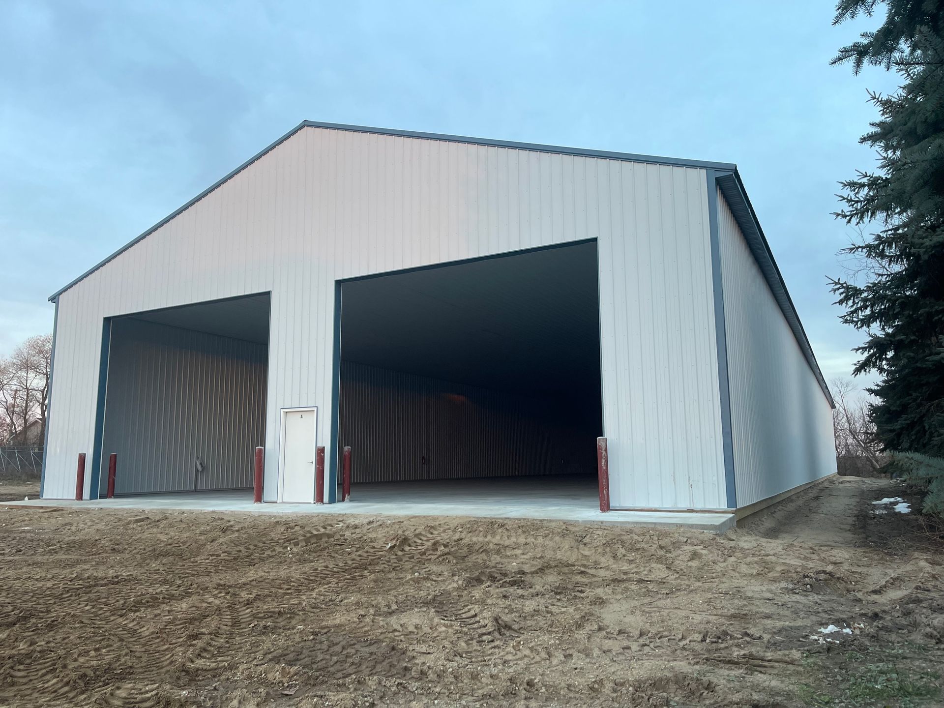 White metal agricultural building with two large openings under a cloudy sky.