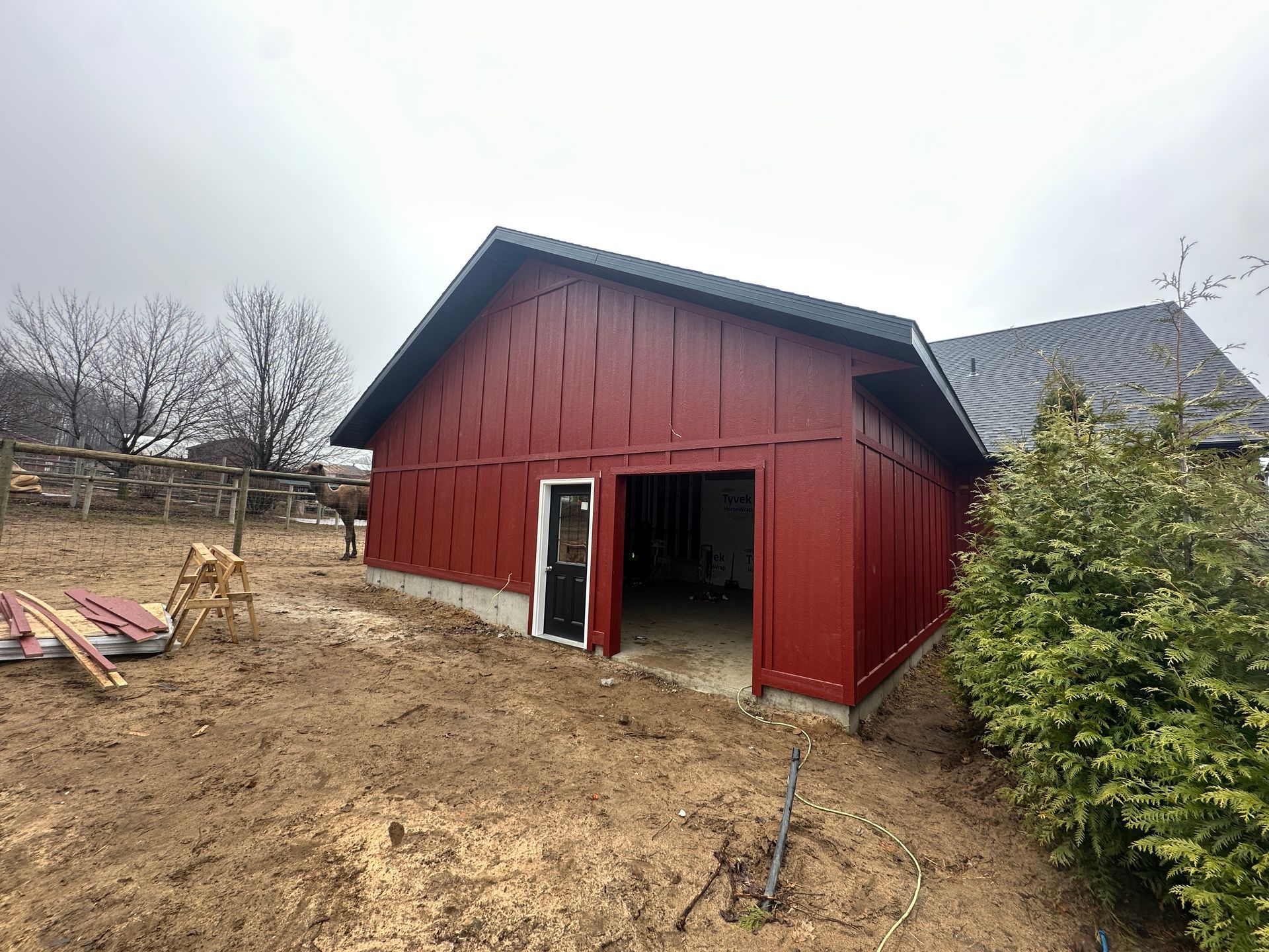 Red barn-style building with a black roof and an open doorway on a dirt lot.