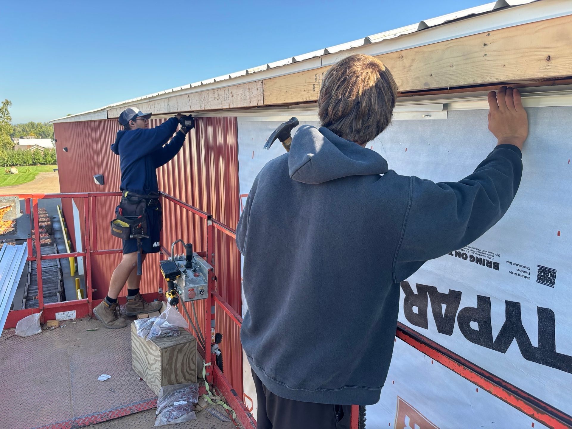 Two construction workers installing siding on a red building's exterior.