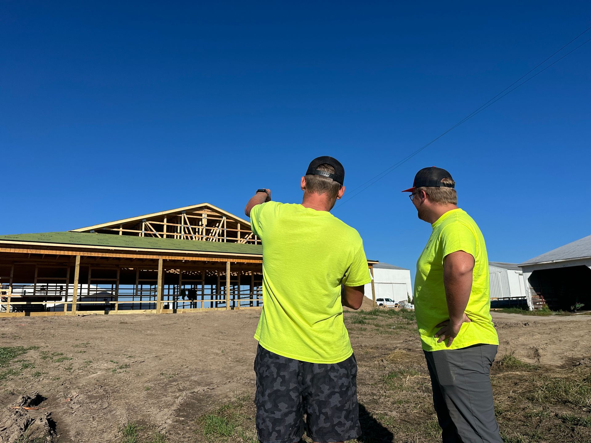Two men in neon shirts discuss construction progress on a sunny day.