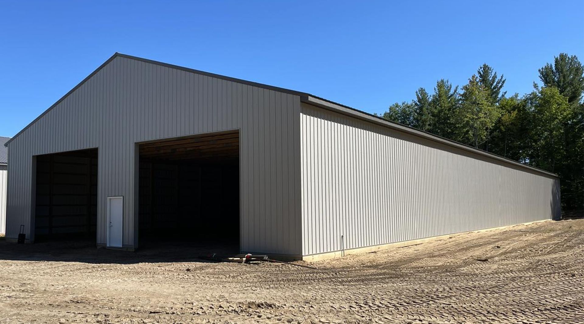 Gray metal barn with two open bays, clear blue sky.